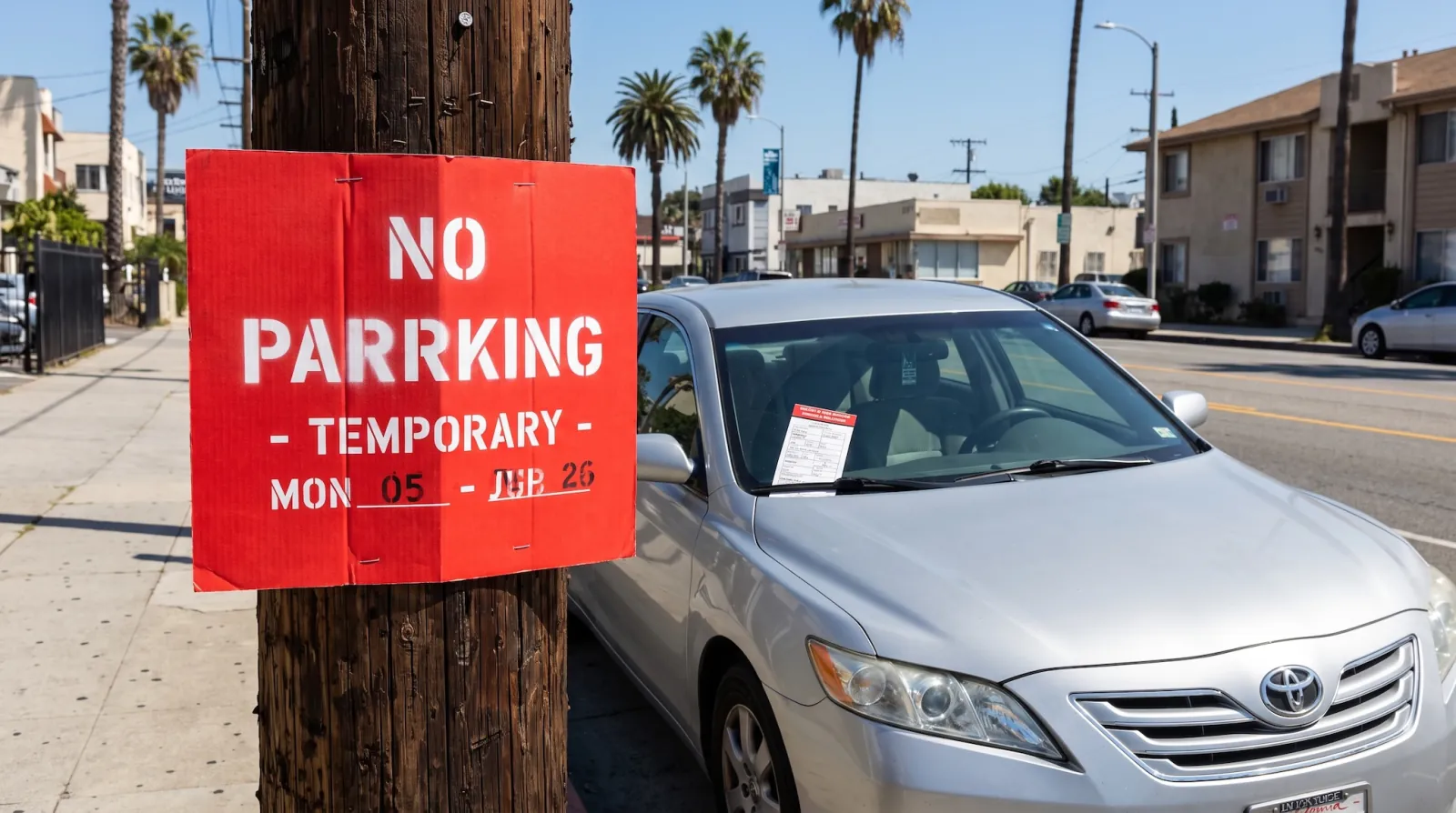 A temporary paper No Parking sign taped to a pole on an LA street